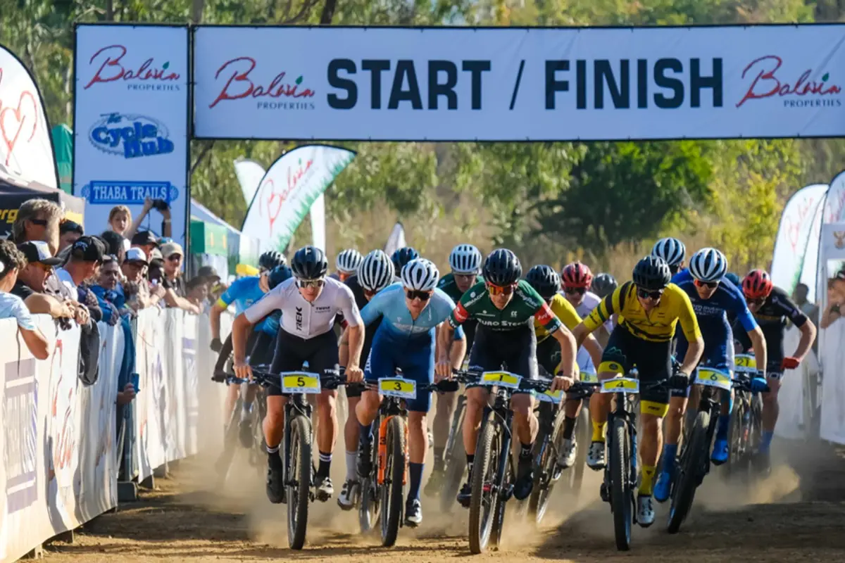 MTB cross-country (XCO) mass start beneath a Start/Finish banner, Gauteng juniors kicking up dust at Thaba Trails.