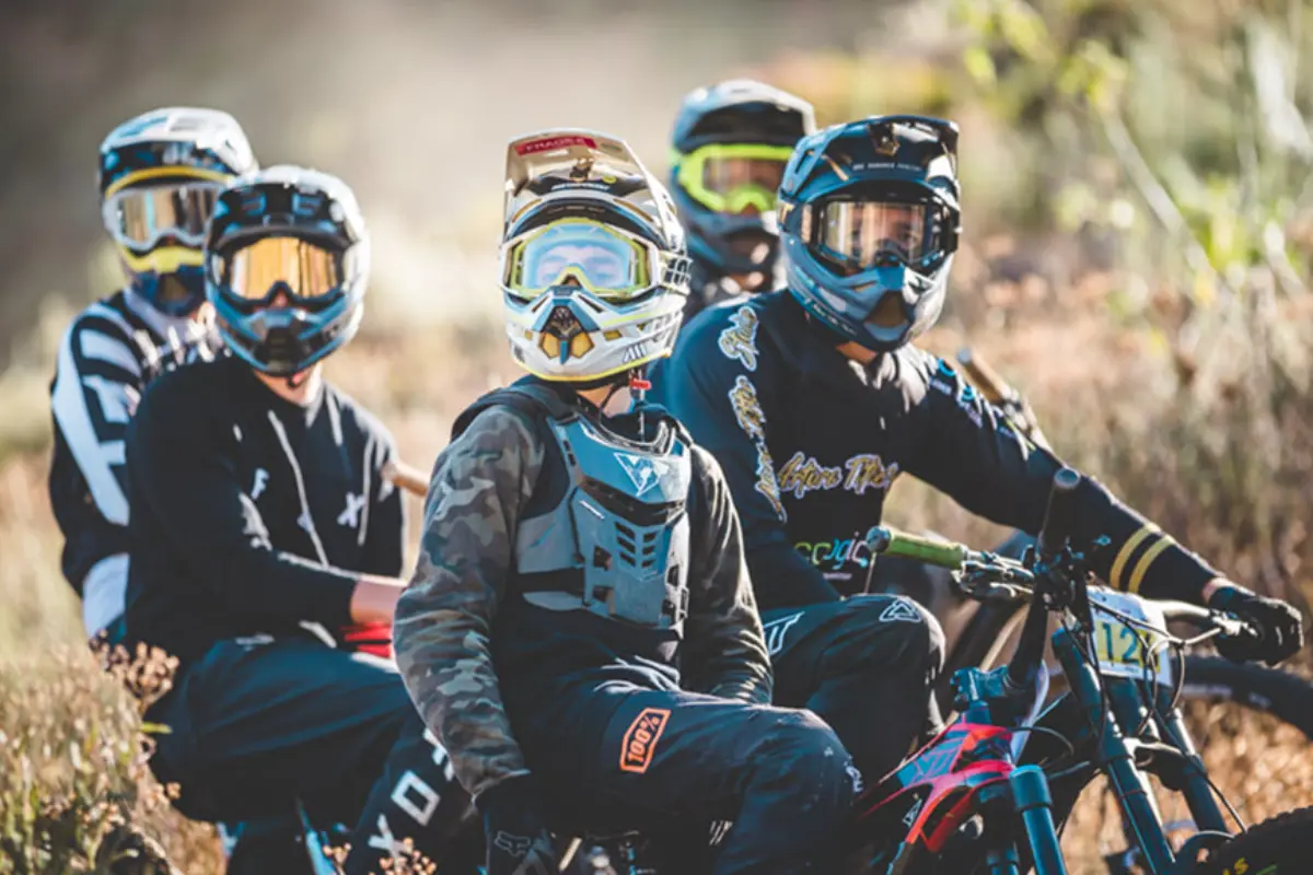 Group of downhill mountain bikers in full-face helmets and body armour waiting with their bikes at the top of the course.