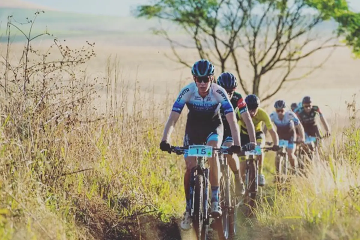 MTB marathon (XCM) lead group riding singletrack through tall grass, rider 15 at the front.
